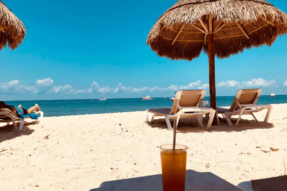 A photograph captures the serenity of a calm beach on a sunny day, with a cocktail glass in the forefront framing the tranquil seascape.