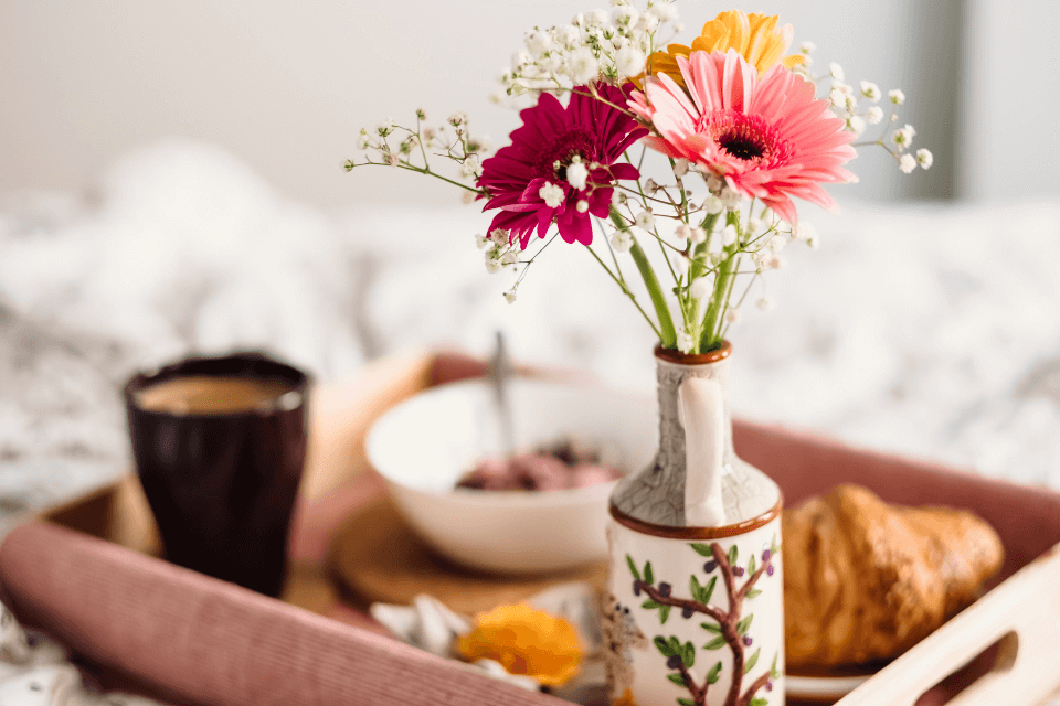 breakfast in bed photographed from up close with a flower vase in the forefront focus