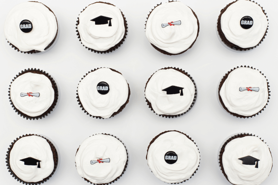 A photograph taken from a high angle view showcasing a selection of beautifully decorated graduation cupcakes. The image captures the intricate details and festive designs of the cupcakes