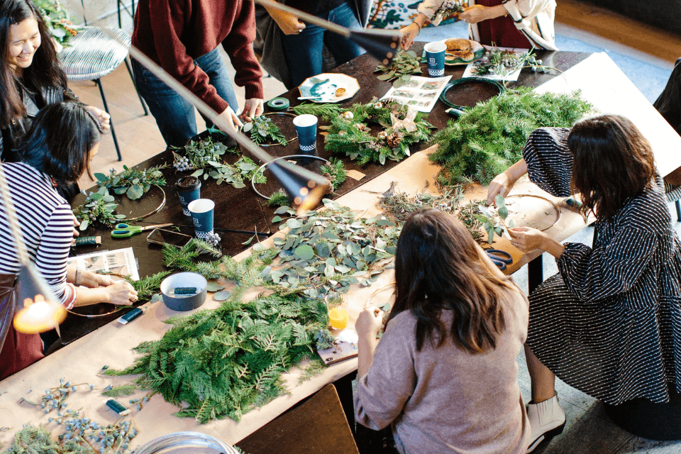 Women gathered together for a crafting session, creating beautiful wreaths from fresh leaves and flowers, immersed in creativity and companionship.