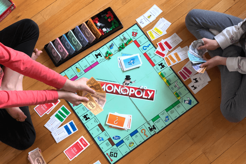 Two women engaged in a friendly game of Monopoly, moving pieces and exchanging currency on the iconic board game.