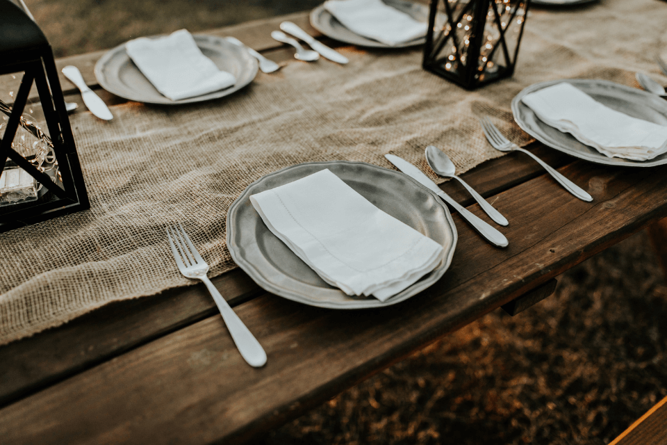 A table set for a special occasion, featuring lantern centerpieces casting a warm glow, with neatly arranged plates, forks, and spoons, ready for the event to begin.