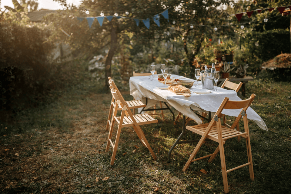 A rustic table set for a wine tasting party in an outdoor setting, with wooden chairs and a spread of gourmet food inviting guests to savor and celebrate.