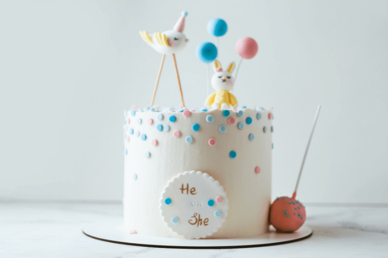 Pastel birthday cake featuring a bunny, bird, and balloons, with 'He' or 'She' in marzipan. Ideal for gender reveal or baby shower celebrations. Soft hues evoke tenderness and innocence. cover for Gender Reveal Party Ideas blog post