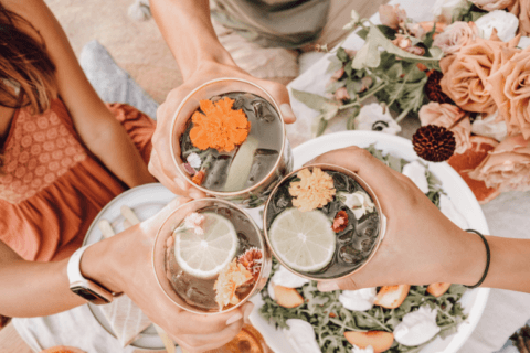 Joyous bachelorette party scene: Friends raise glasses with drinks adorned with lemon slices and flowers. A lively celebration captured, radiating camaraderie and happiness.