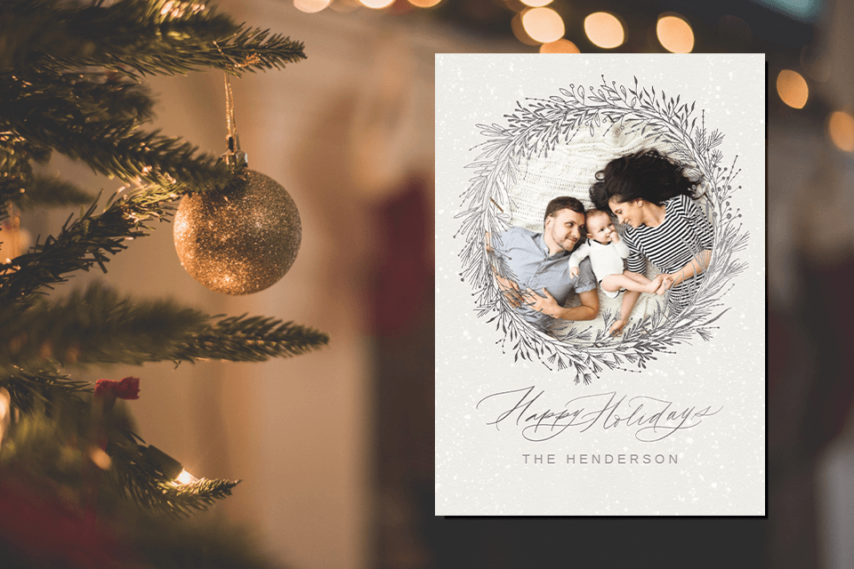 Warmest Holiday Wishes! A Chic 'Happy Holidays' in Graceful White and Grey Script. Centered Family Photo Embraced by an Illustration of a Festive Christmas Wreath. All Against the Backdrop of a Gleaming Christmas Tree Bedecked with Lights and Ornaments.