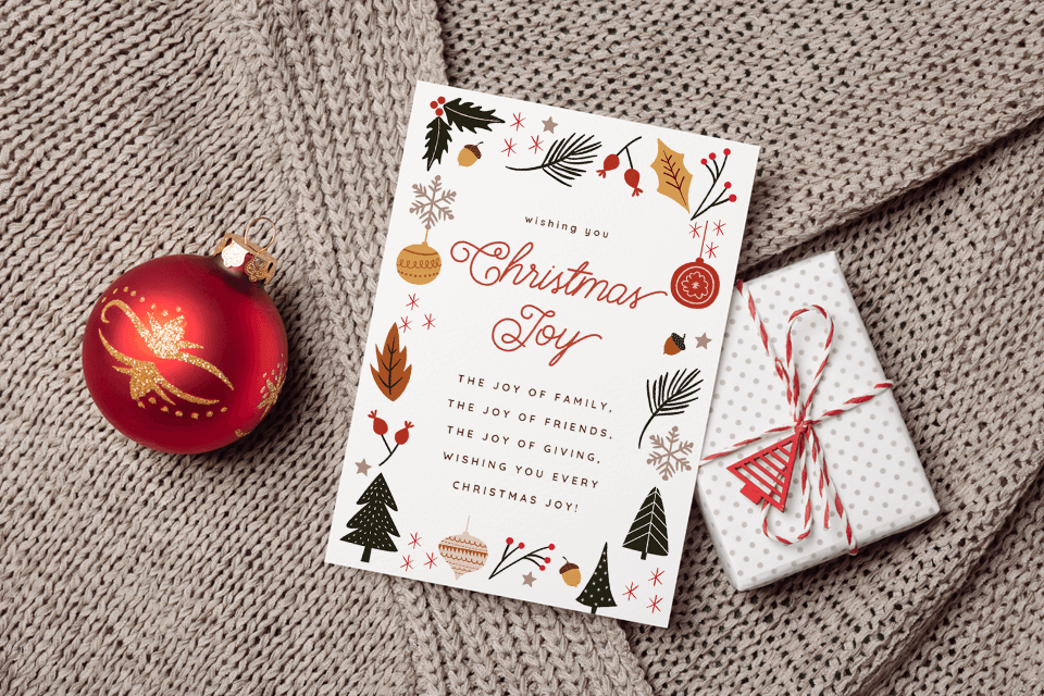 Wishing You Christmas Joy! An Elegant Greeting in Dark Orange, Surrounded by Illustrated Festive Elements: Ornaments, Pine Tree Branches, and American Holly. Adjacent to a Red Ornament and a Wrapped Gift Resting on a Cozy Sweater.