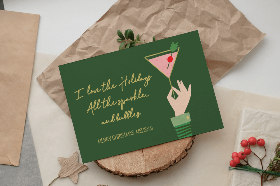 Green Christmas card: 'I love the Holidays. All the sparkle... and bubbles. MERRY CHRISTMAS!' Illustrated hand holding a martini glass with a cherry on top, displayed on a wooden stand.