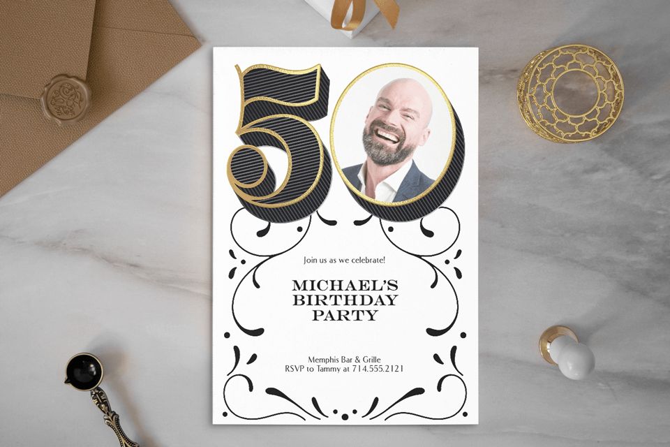 Elegant white 50th birthday party invitation featuring the number 50 with a person's image inside the zero. The background is a granite table surface with strategically placed objects for effect.