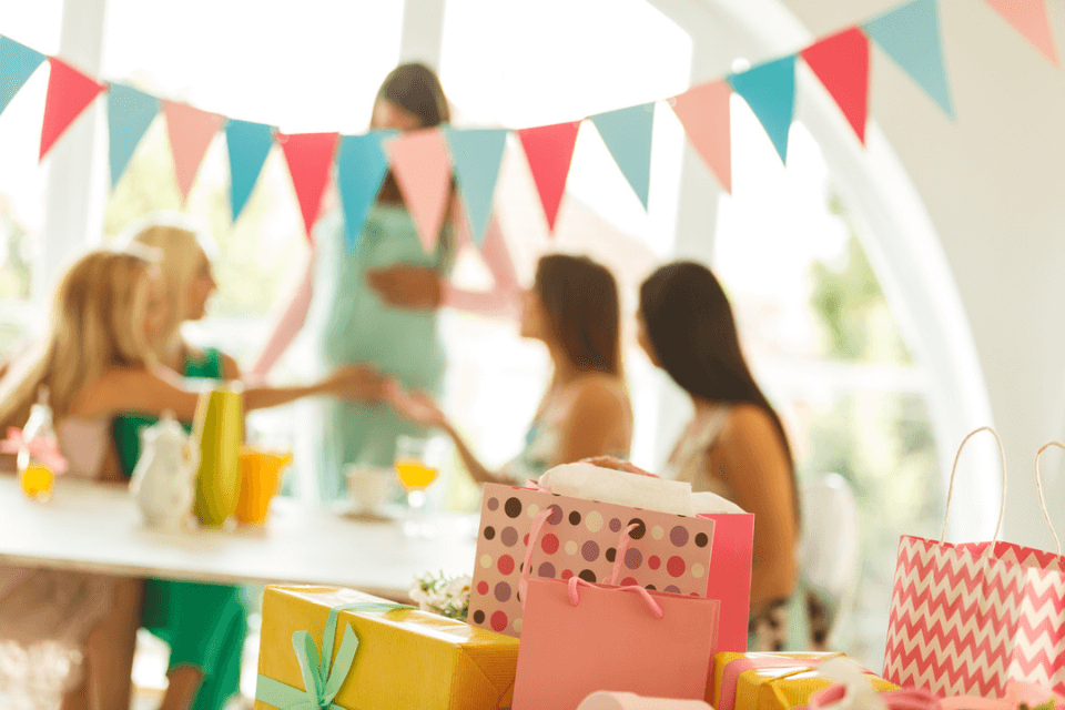 Foreground showcases a collection of beautifully wrapped baby shower party gifts, with a joyous woman celebrating in the background, adding to the festive atmosphere.