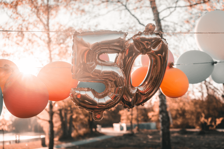 Cover for blog post Special 50th Birthday Party Ideas for an Amazing Celebration featuring Two silver number 50 balloons tied together with a silver ribbon, floating against a blue sky with white clouds.