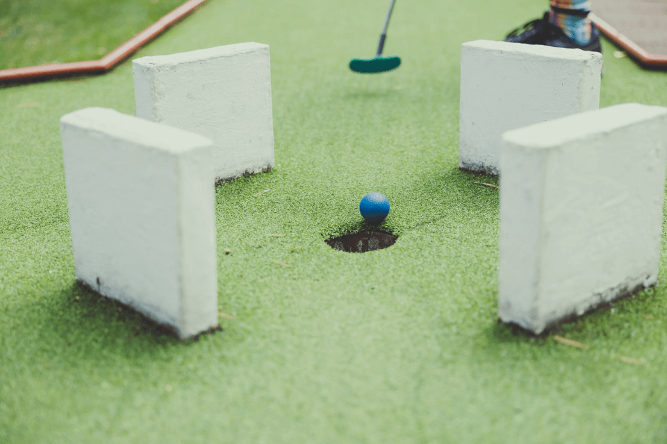 Experience Birthday Bliss: Mini Golf Extravaganza with Friends! A Player Expertly Guides a Blue Ball Through Challenging Barriers, Nailing the Perfect Shot into the Hole.