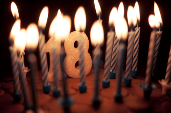Close-up of a vibrant 18th birthday cake with glowing candles shaped as the number 18 and a lot of smaller lit candles circling the number 18, set against a festive backdrop, cover for blog post 'Epic 18th Birthday Party Ideas: 20 Unique Themes to Make Your Celebration Shine'
