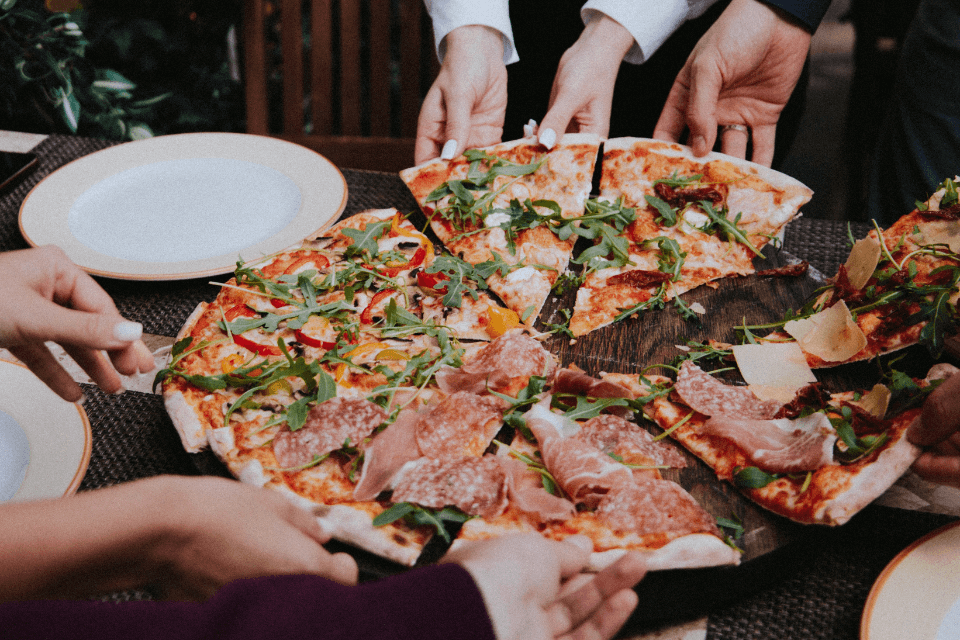 Enthusiastic Guests Reaching for a Selection of Flavorful Pizza Slices on Wooden Stand at Vibrant Teen Birthday Party Celebration