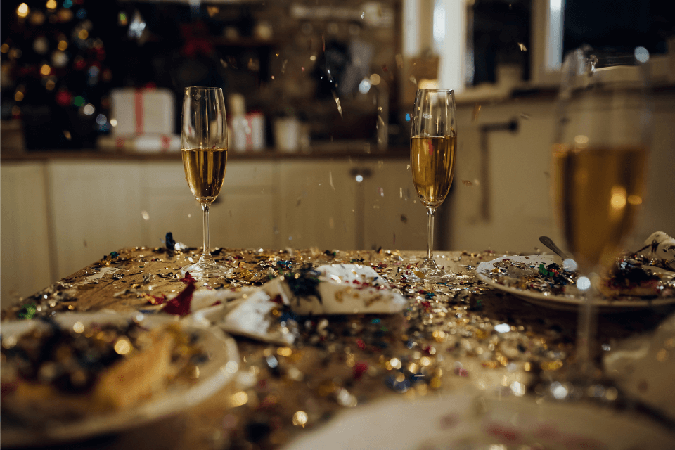 A New Year's Eve party table lavishly adorned with confetti, sparkling champagne glasses, and elegant plates, setting a festive and celebratory atmosphere.