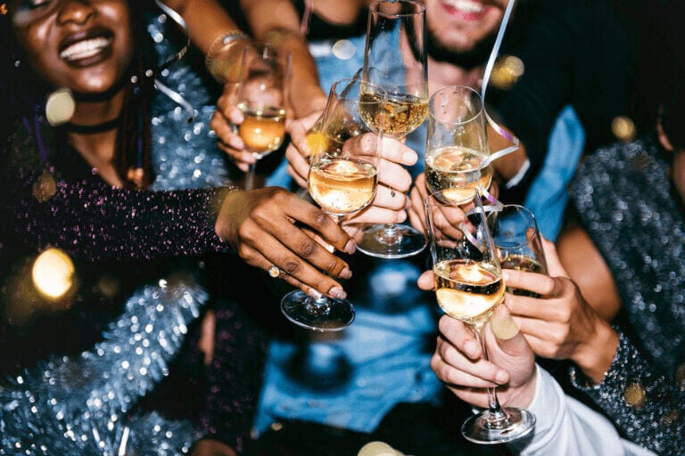 Festive New Year Celebration: Joyful individuals adorned in colorful attire raise their champagne glasses in cheerful toast, enveloped in an atmosphere of happiness and merriment as they ring in the new year.