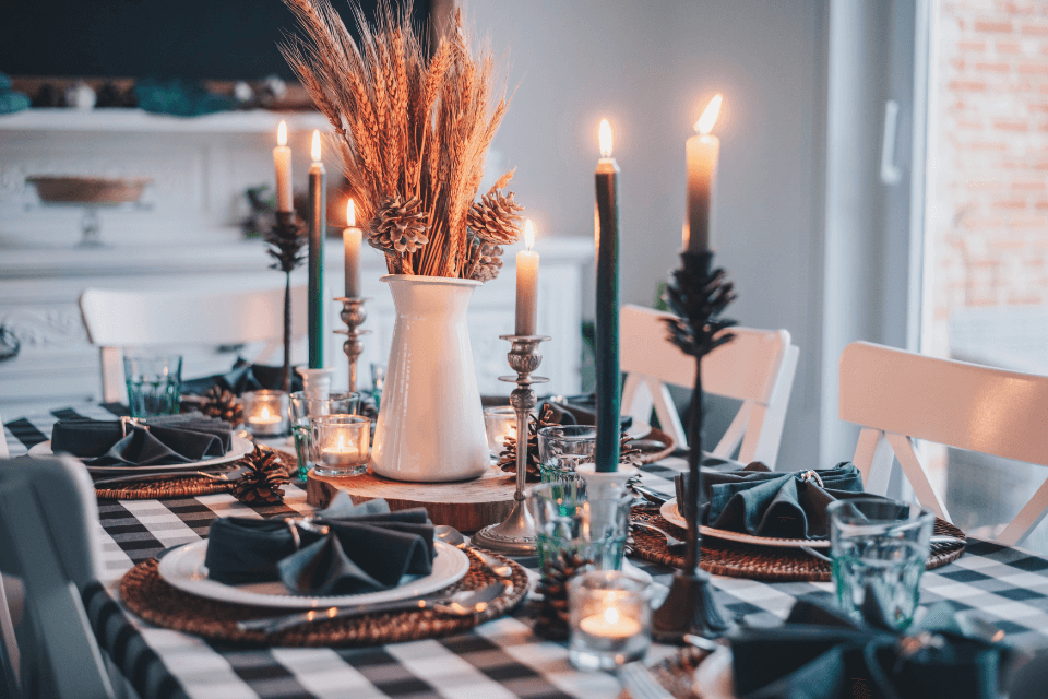 An elegant and cozy dinner party table setting featuring lit candle centerpieces, winter flowers, and a black and white tablecloth.