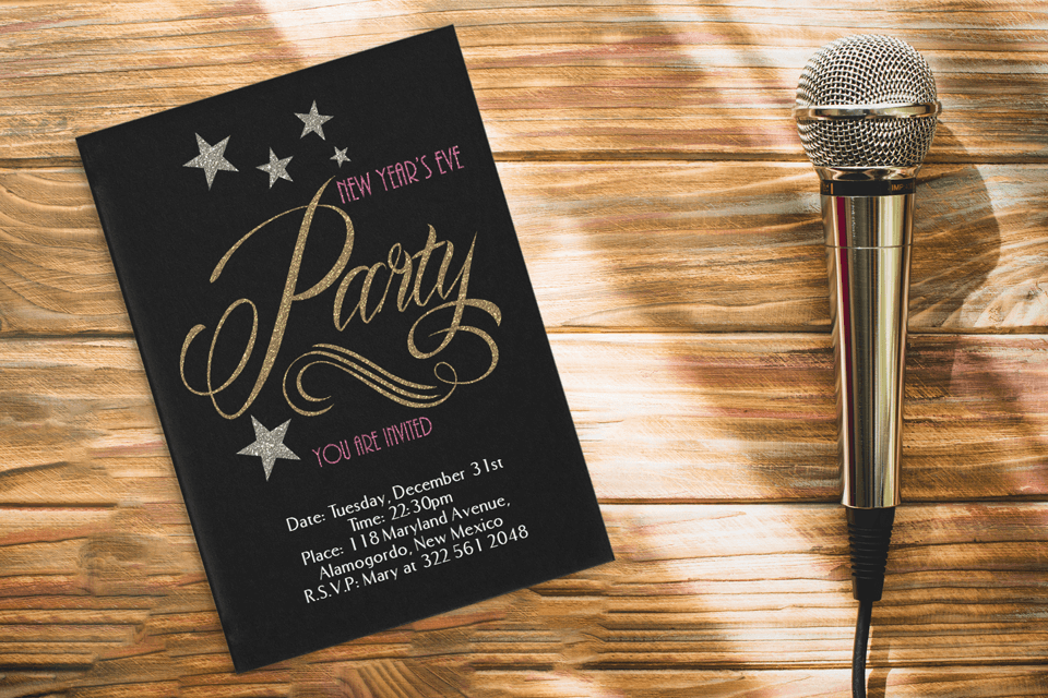 A New Year's Eve party invitation designed in black and gold, with pink text accentuated by sparkles and star illustrations, highlighting a karaoke night theme. The invitation rests on a wooden surface, near a karaoke microphone