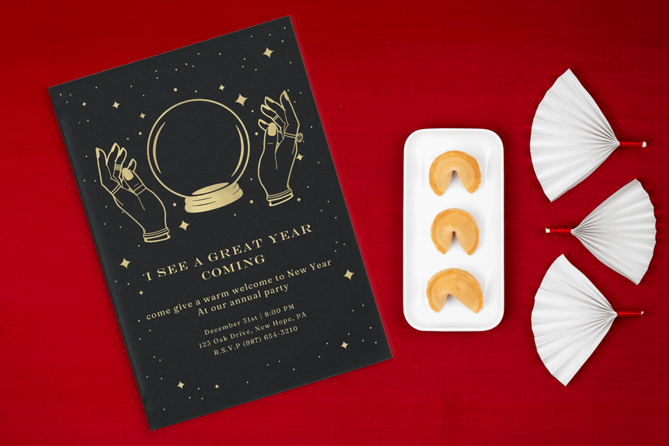A black and gold invitation with the phrase 'I See a Great Year Coming'. It features an illustration of hands encircling a crystal ball, which sits on a red surface beside fortune cookies, adding a mystical and hopeful theme to the New Year's celebration.