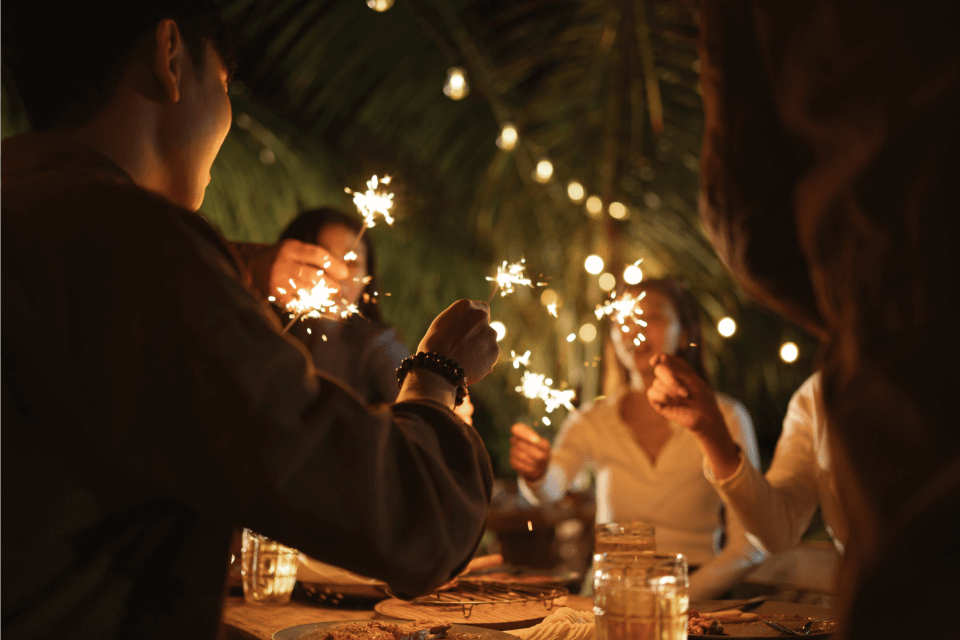 A group of people gathered around a table at a New Year's Eve party, each holding lit sparklers, creating a festive and joyful ambiance.