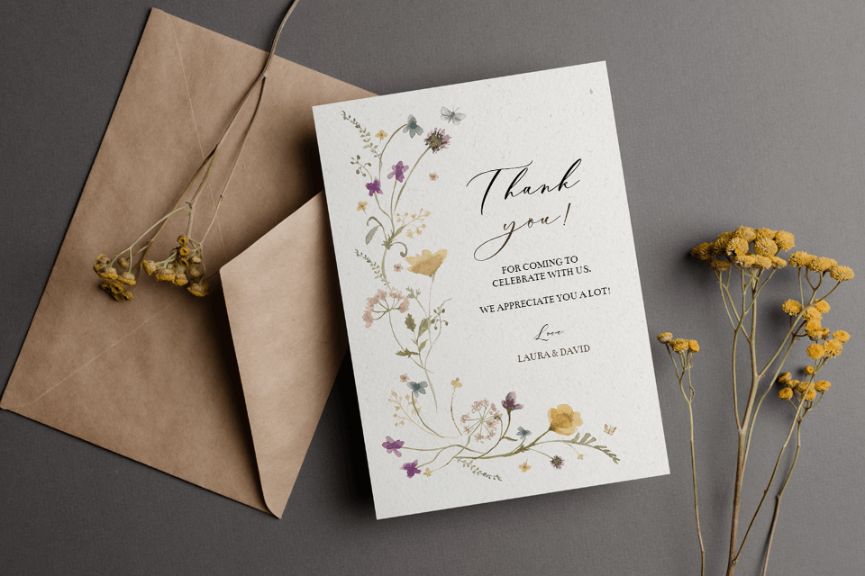 A simple yet elegant thank you card adorned with a floral illustration, placed beside an envelope, accompanied by small, delicate yellow flowers.