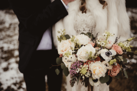 A joyful newlywed couple captured in an outdoor winter setting, epitomizing the bliss of a winter wedding. Bride and groom in the background, in the foreground the bride's elegant bouquet adds a touch of color and charm to the snowy landscape.