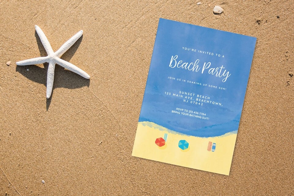 A vibrant beach drawing unfolds, showcasing sun-kissed sand, turquoise waves, and colorful umbrellas from above. An invitation to a beach picnic birthday rests on the sand beside a starfish, promising a fun-filled celebration