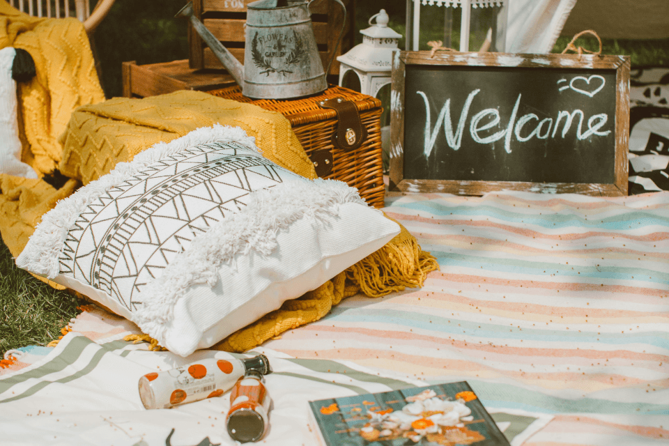 An intimate and stylish celebration unfolds with a small, elegantly laid picnic adorned with charming decor, nestled amidst comfortable pillows and cushions. 