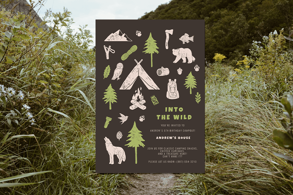 A sprawling grassland landscape sets the stage for an adventurous birthday celebration. The invitation, adorned with 'Into the Wild' and illustrations of forest animals and camping gear, rests on top, promising an outdoor escapade filled with excitement