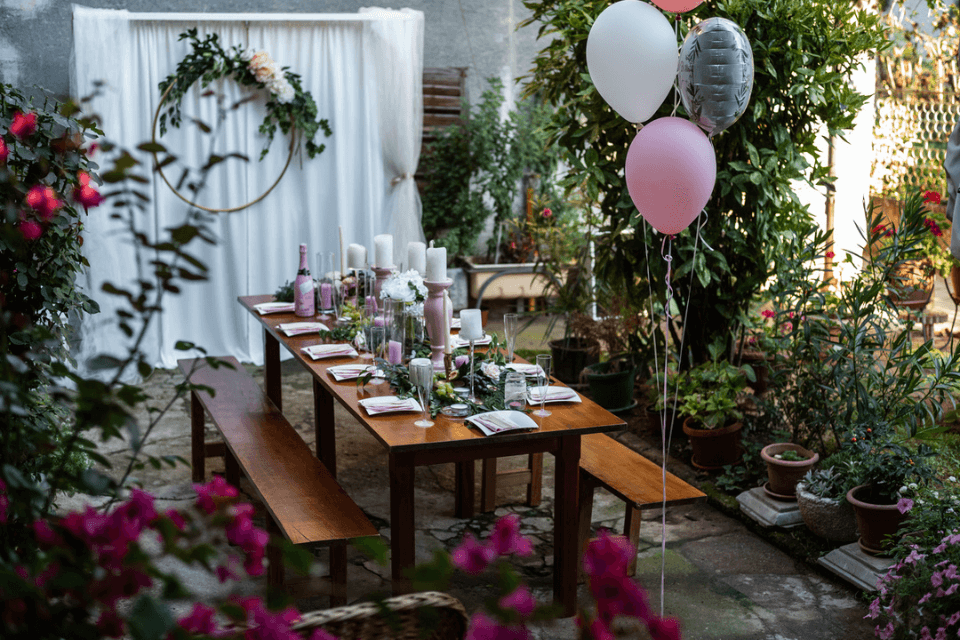 transforming the outdoors into an enchanting setting for a bridal party shower, the elegantly set table is adorned with whimsical balloons, candle tablepieces casting a soft glow, and lush greenery, creating a captivating ambiance of celebration and joy
