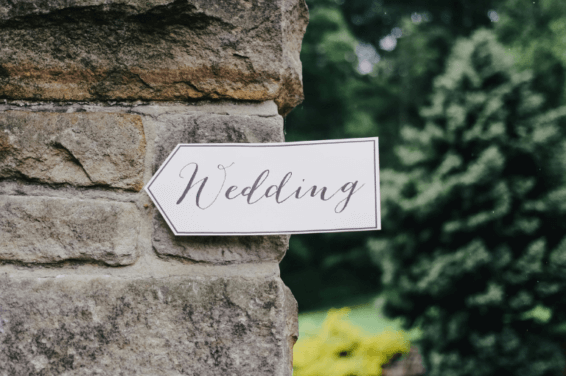 Rustic wedding signage: A charming arrow-shaped pancart with 'Wedding' elegantly scripted, adorning a textured stone wall, guiding guests towards the joyous celebration.