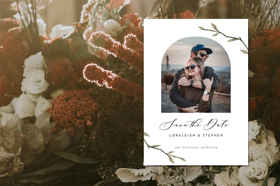 Save the date card exuding simple elegance, adorned with a charming illustration of the couple framed by two delicate branches, all set against a backdrop of assorted blossoms