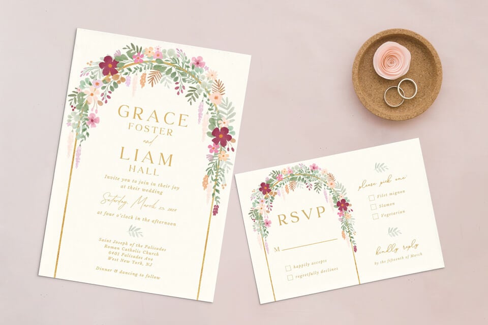 Invitation to a floral-themed wedding with RSVP. A delicate flower arch gracefully frames the text, mirroring the floral motifs. Adjacent, a wooden holder displays two rings alongside a dainty pink rose.