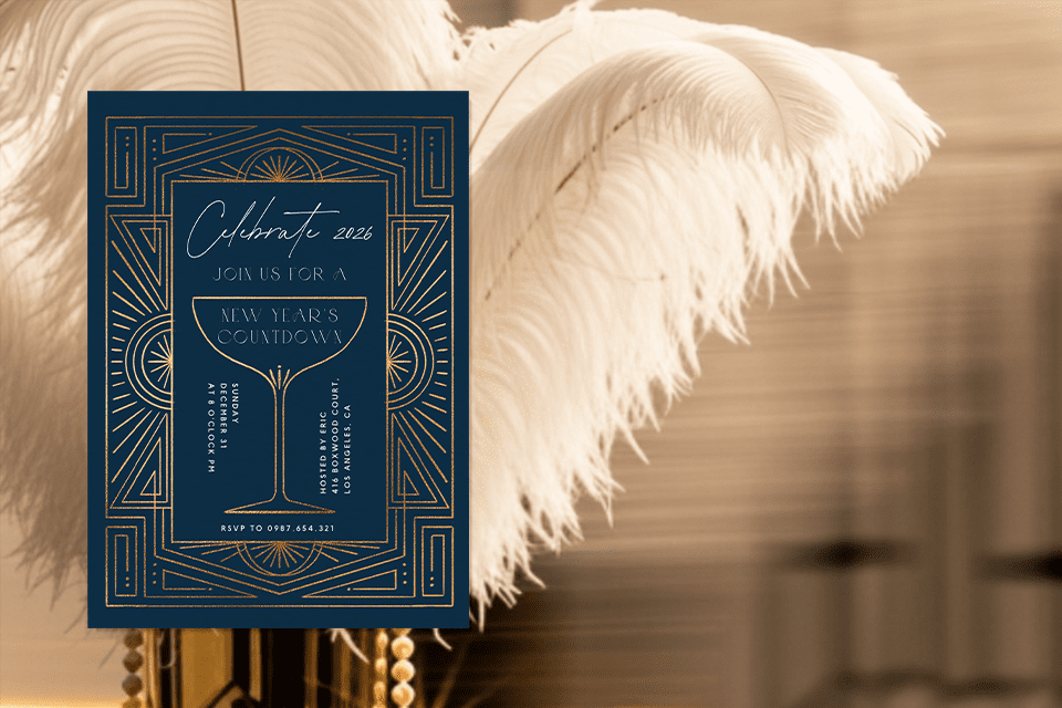 new-gatsby-style-new-year-theme-party-invite A navy-blue Art Deco New Year’s Eve invitation with gold geometric linework and a central gold-outlined champagne glass. The text reads ‘Celebrate 2026’ and includes party details. The card is displayed in front of soft, cream-colored ostrich feathers.