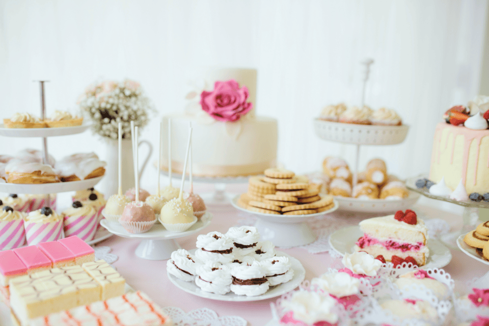 quinceañera food table cakes cupcakes birthday (1) Elegant dessert table with a white tiered cake, cupcakes, cake pops, cookies, pastries, and pink-accented sweets arranged on stands for a celebration.