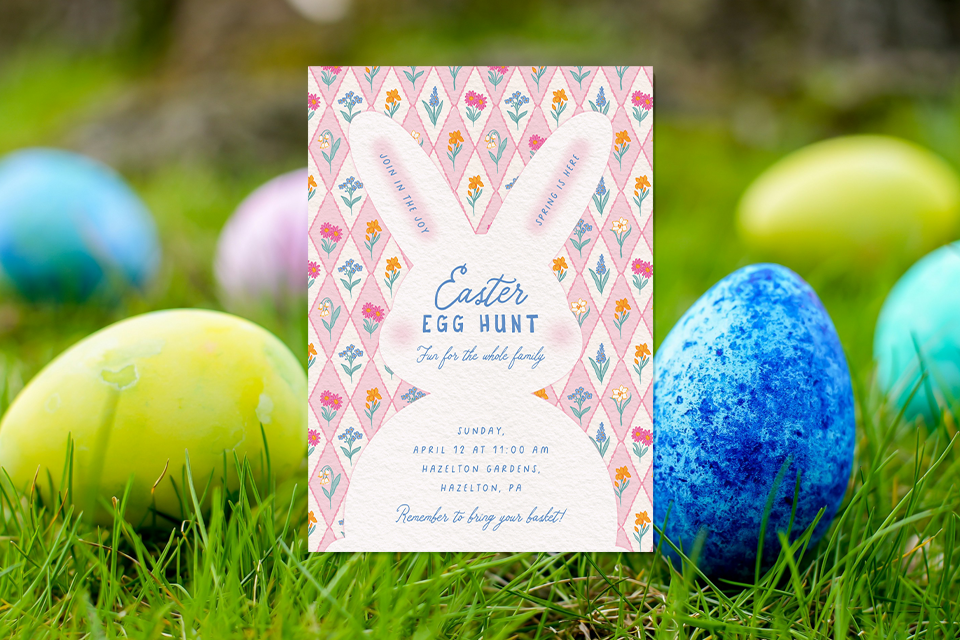 egg-roll-activity-egg-hunt-easter-invite-bunny Easter egg hunt invitation with a bunny-shaped design and floral pattern, placed on grass surrounded by brightly colored Easter eggs.